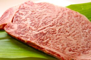 Close-up of a raw A5 Wagyu steak, richly marbled, placed on a green leaf
