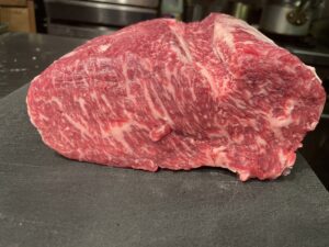 Raw Akaushi Wagyu steak resting on a dark slate counter, showcasing its deep red color and delicate marbling.
