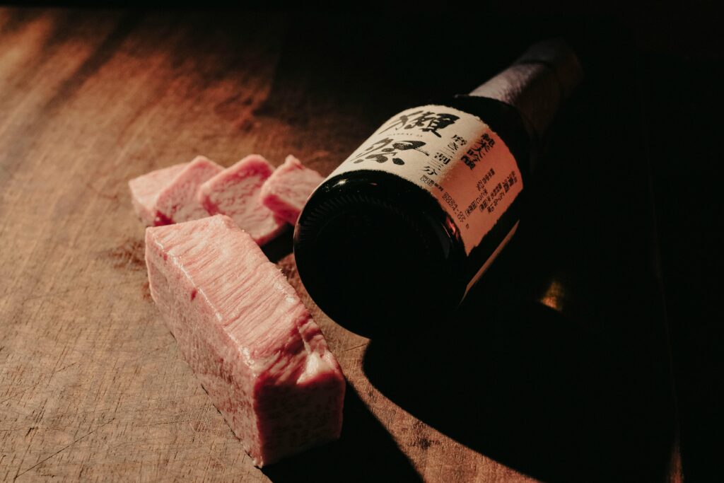 Sliced Wagyu beef and a bottle of red wine on a wooden table, representing a premium dining experience in Tokyo.