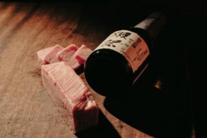 Sliced Wagyu beef and a bottle of red wine on a wooden table, representing a premium dining experience in Tokyo. 